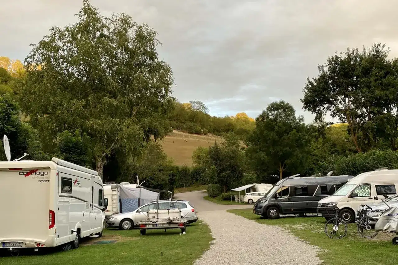 Wohnmobile und Autos auf einem Campingplatz bei Rothenburg ob der Tauber. Im Hintergrund sanfte Hügel mit Bäumen.