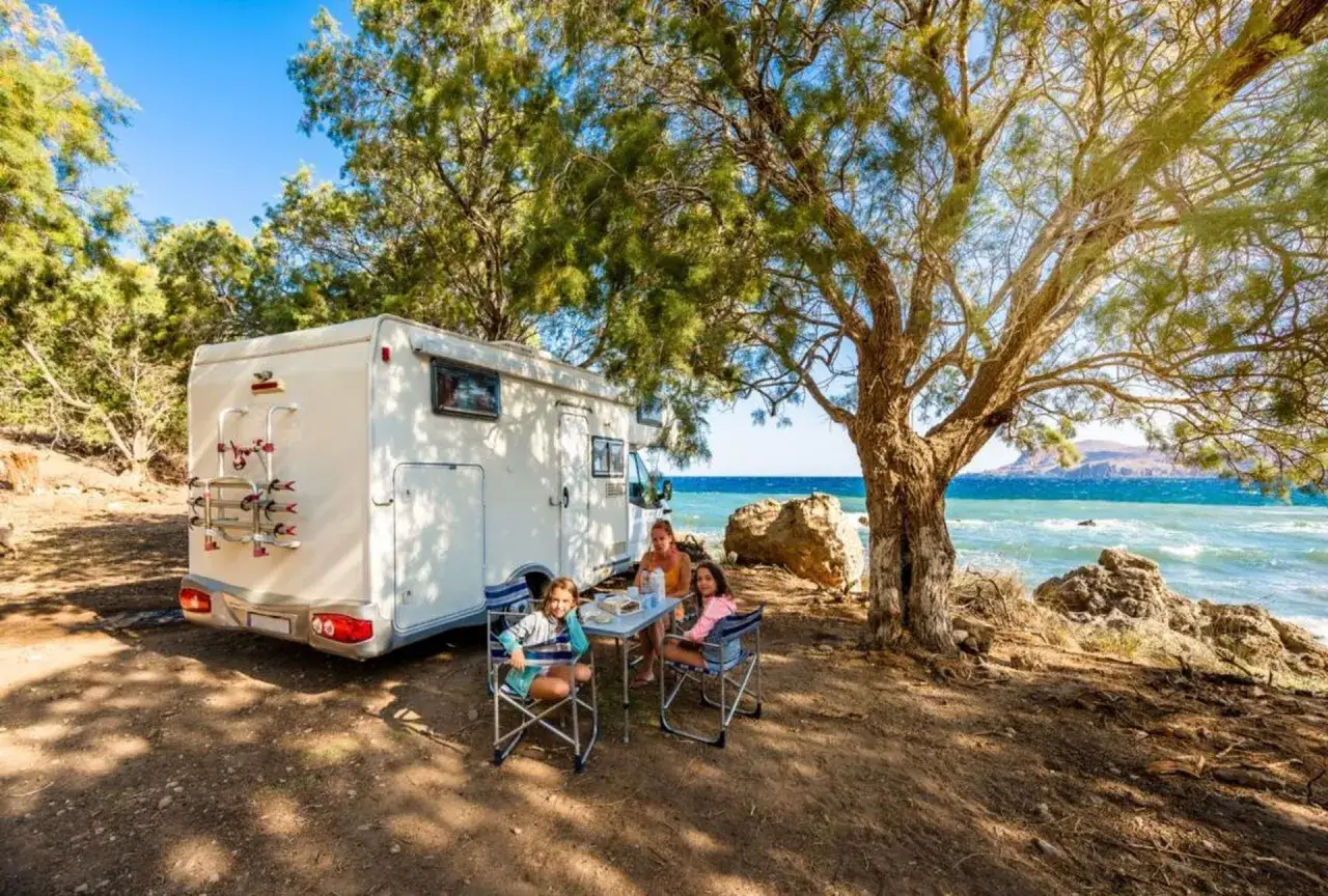 Familie genießt sonniges Wetter auf Sardinien im Oktober. Wohnmobil am Meer, Kinder sitzen am Tisch.
