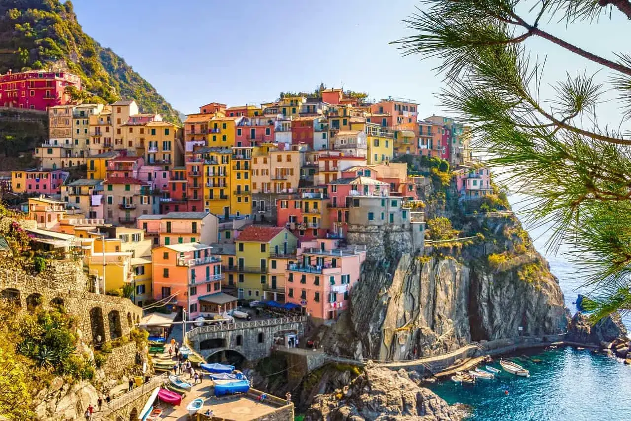 Bunte Häuser schmiegen sich an steile Klippen in Cinque Terre. Boote liegen im türkisfarbenen Meer.